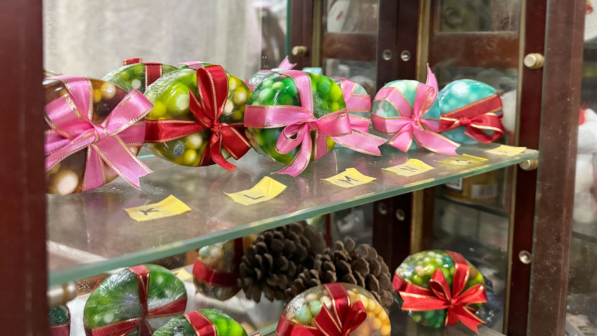 ハンドメイドの仕事の成果物の写真。透明でカラフルな、だ円形の手作り石けん(雑貨)。ビーズ状に小さく丸めた石けんを中に埋め込み、赤やピンクのリボンでラッピングされています。